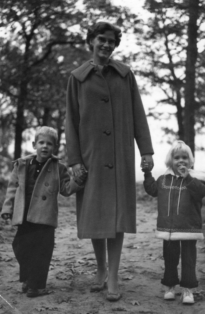 black and white image woman in long coat sanding outside with a young boy and girl on either side