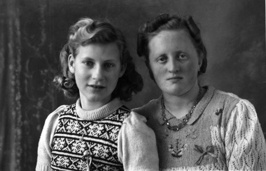 black and white portrait girl with shoulder length curled hair and pattened sweater vest sitting next to older woman with short curled hair and floral sweater